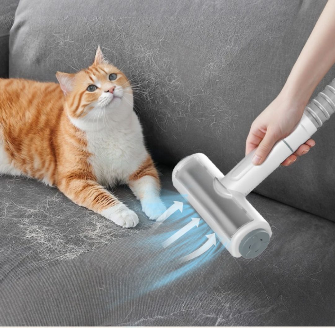 The pet hair roller lifting cat hair off a grey sofa, with a ginger cat watching